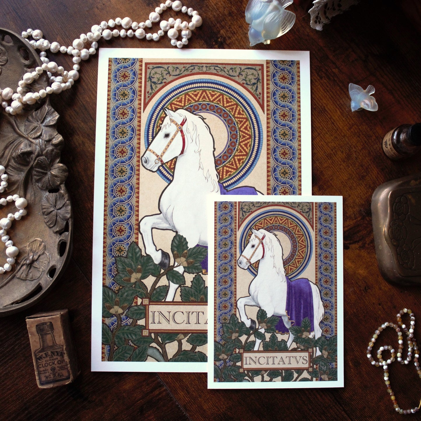 Two prints featuring white horses with decorative borders on a wooden surface.