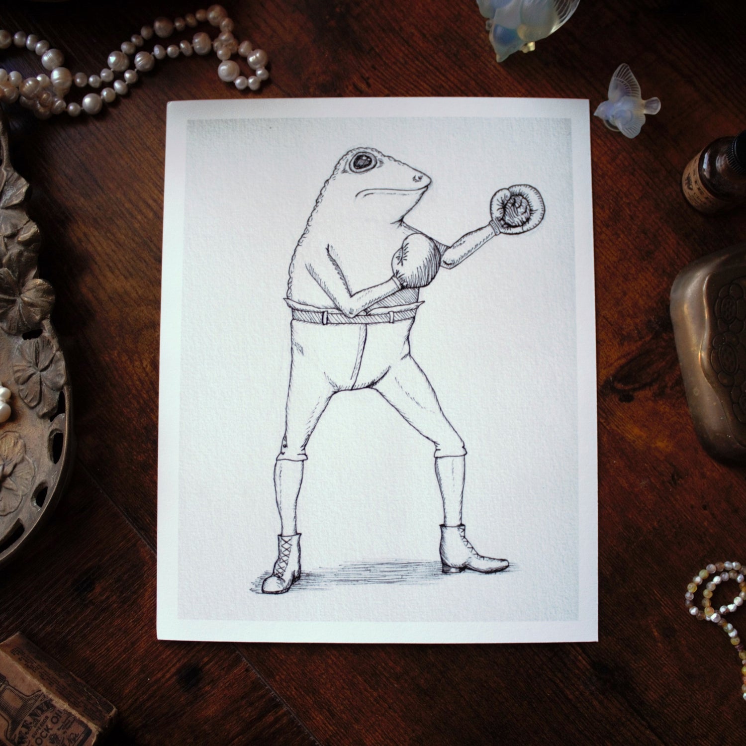 Illustration of a frog in a Victorian boxing pose on a wooden surface with decorative items.