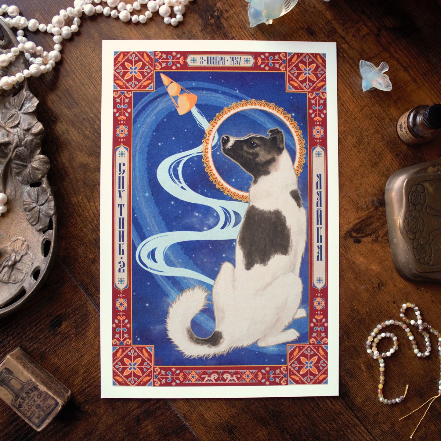 An illustration of Laika the space dog on a wooden surface with decorative items