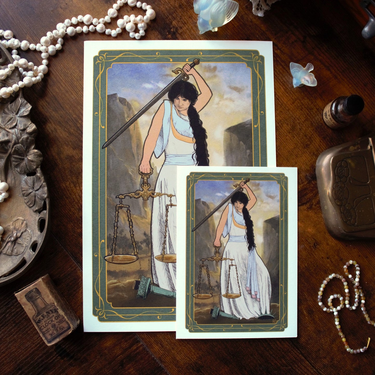 Two prints featuring a woman with a sword and scales on a wooden surface with decorative items.