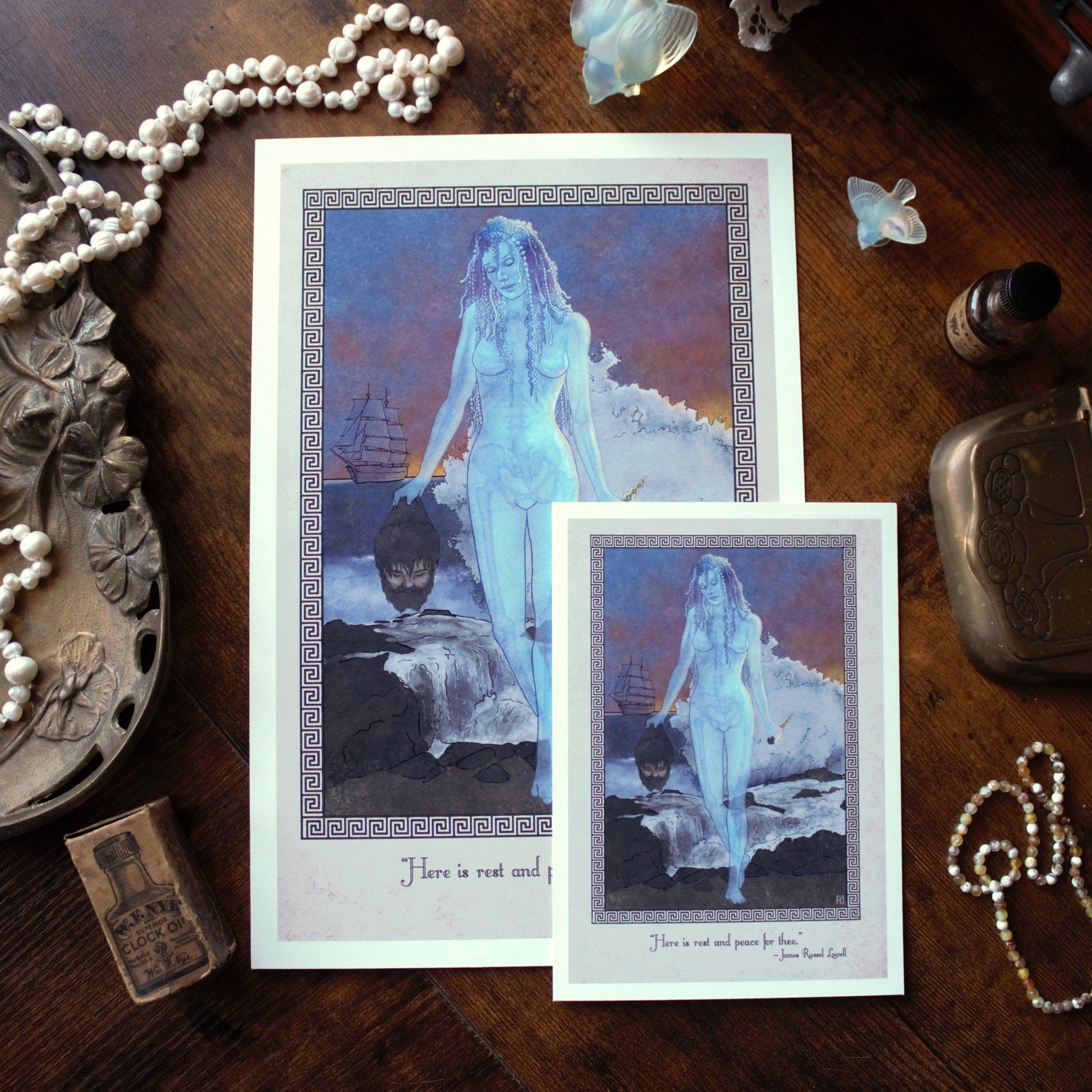 Two prints of Medusa as a jellyfish woman holding Poseidon's head on a wooden surface with jewelry and decorative items.